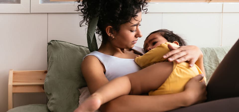 Mother holding and comforting older toddler daughter on bed