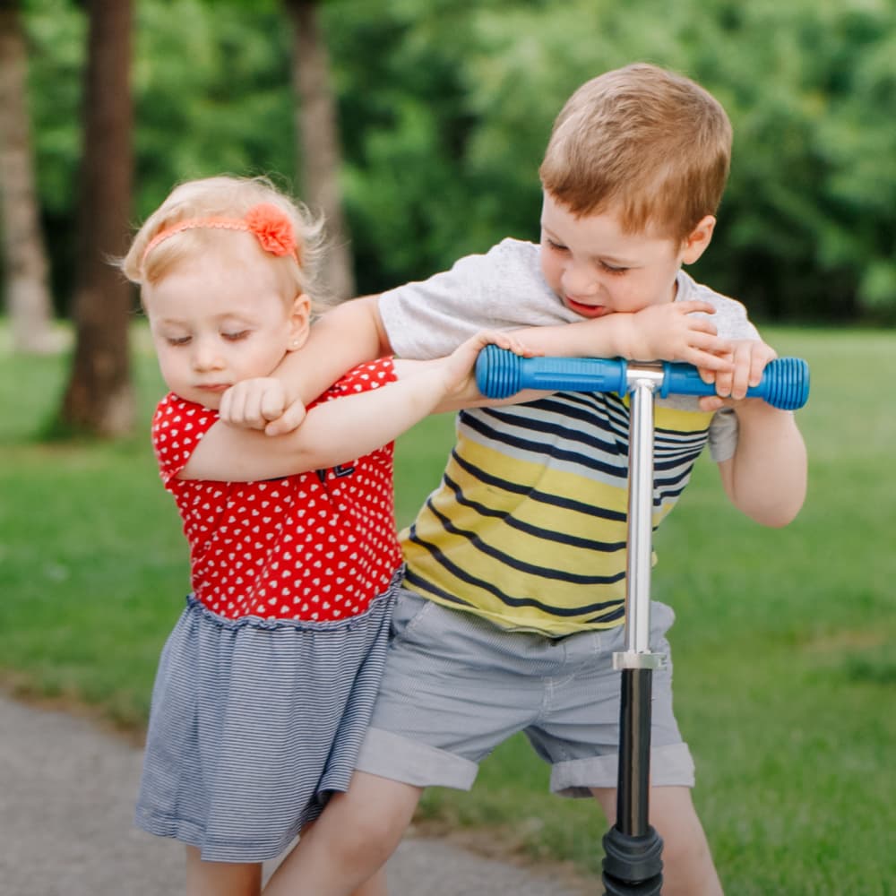 brother and sister siblings in a scuffle while the brother is on a razor scooter