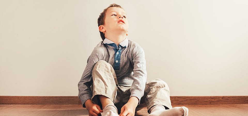 Child sitting on floor putting on socks frustrated going to school