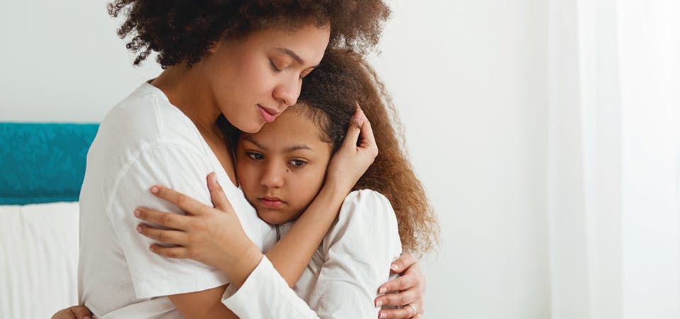 African American mom hugging young daughter after she’s woken up from sleep, scared