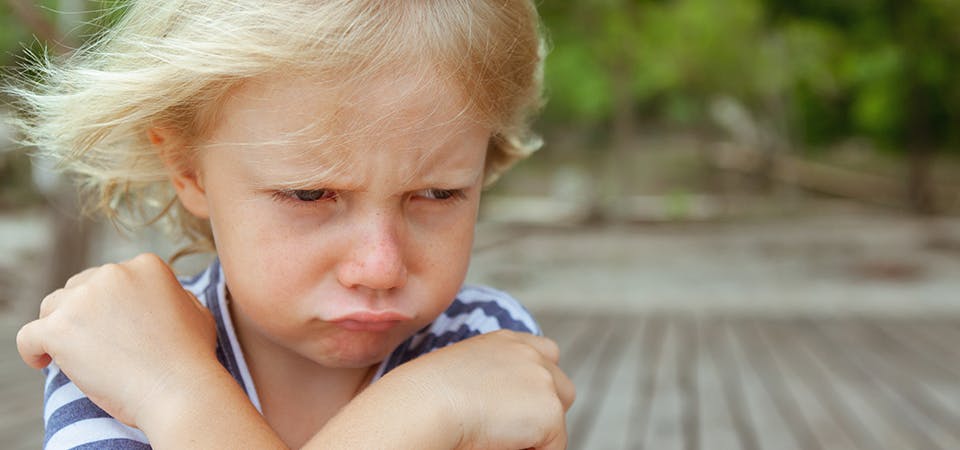 Close up of little blonde girl with arms crossed over her body, pouting and making a whiny face.