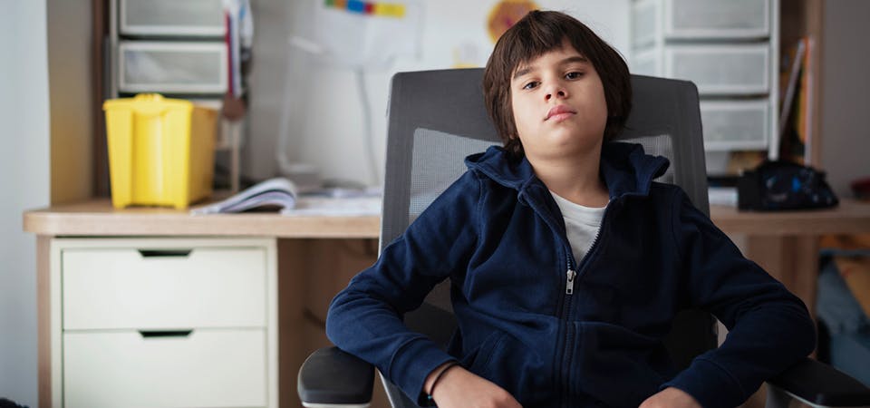 Teen boy sitting in desk chair making a serious face.