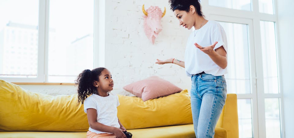 Mom standing and daughter sitting on couch talking about listening, behavior