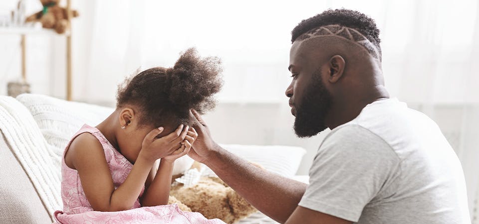 African American father comforting young daughter at home