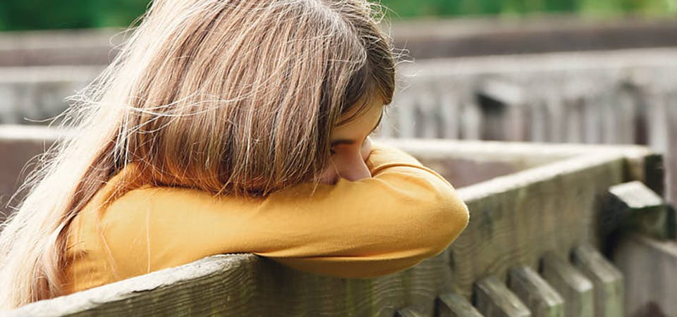 young girl outside covering her face with her arms, looking upset or ashamed