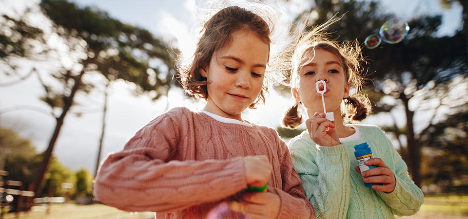 young twin girls playing with bubbles outside