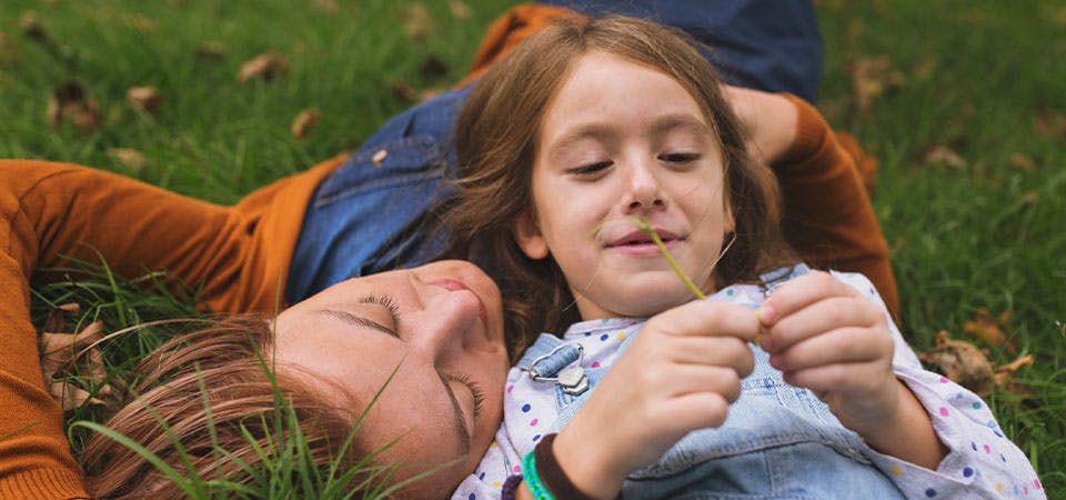 young girl laying with mother in grass, talking and smiling