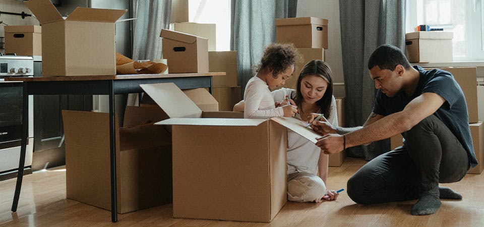 young family sitting among moving boxes, writing on open box together