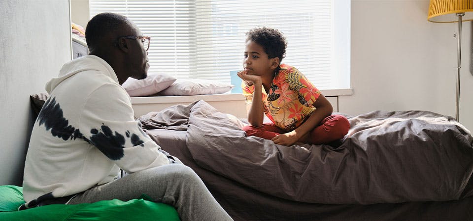dad and young son sitting in bedroom having serious conversation