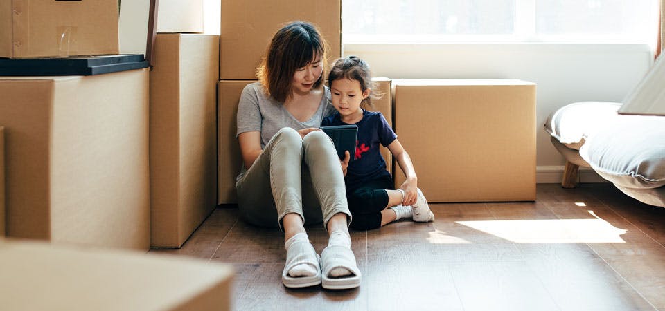mom and young daughter sitting on floor with moving boxes reading book