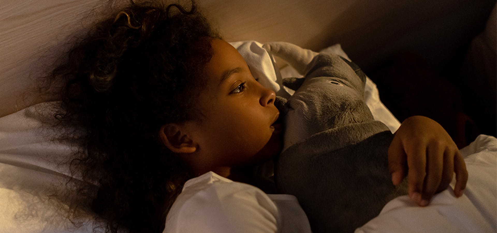Close-up of young girl in bed at night holding stuffed animal and looking away