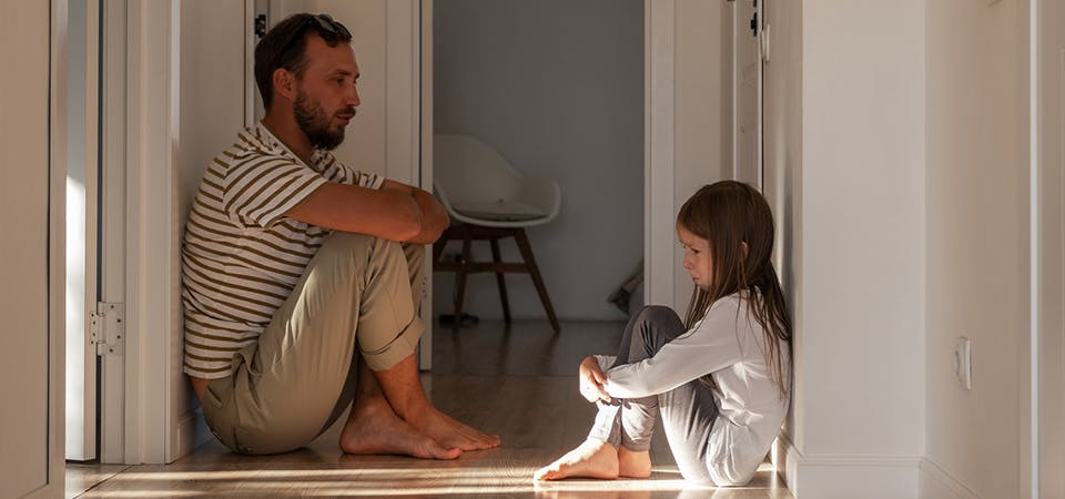 Father sitting on hallway floor with upset daughter